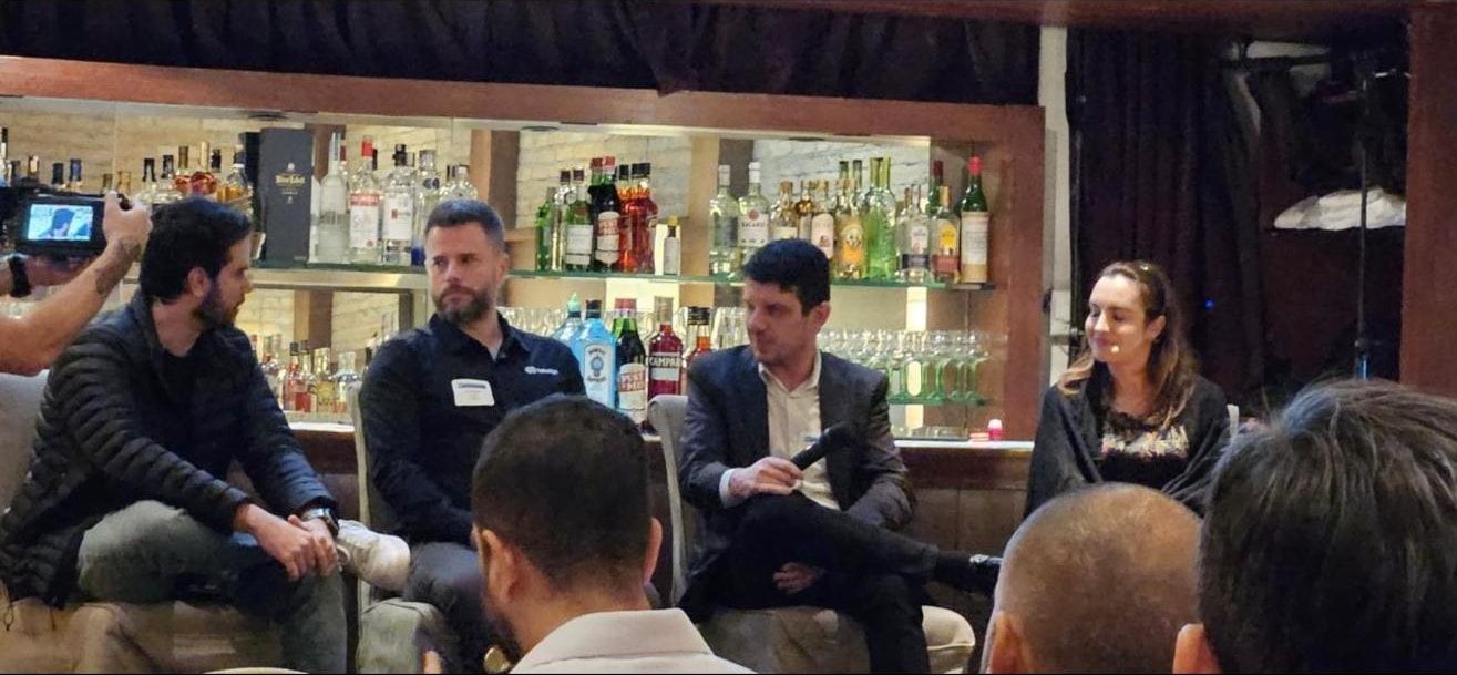 Painel do MRC Connects São Paulo: quatro pessoas sentadas diante de um bar, uma delas com o microfone, e o público em primeiro plano.